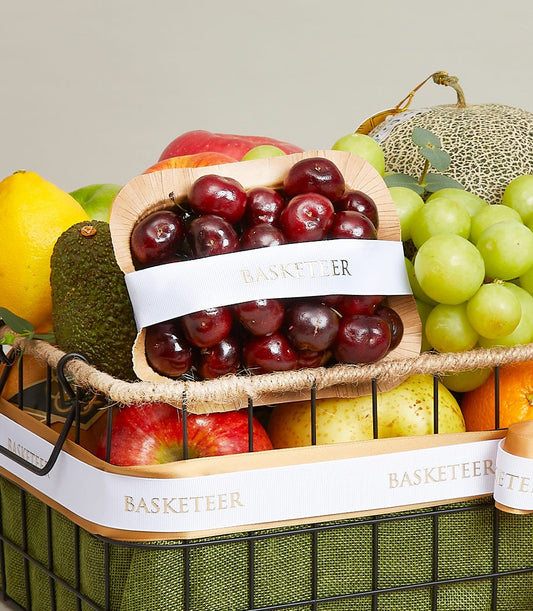 Luxury fresh fruit basket with red cherries, pomelo, avocado, apples, pears, grapes, and cantaloupe in black wire mesh with