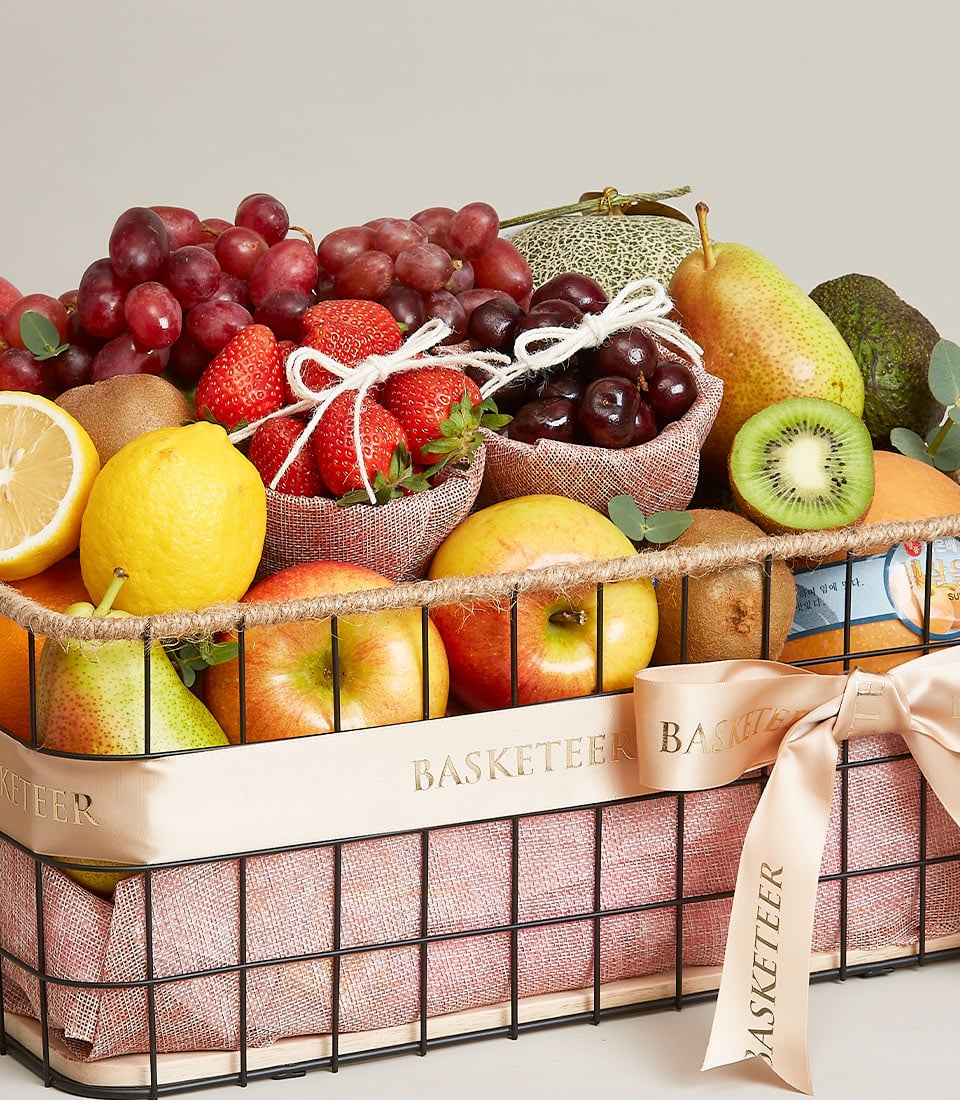 Luxe Fruit Fiesta gift basket with fresh strawberries, grapes, apples, and tropical fruits in black wire frame with peach