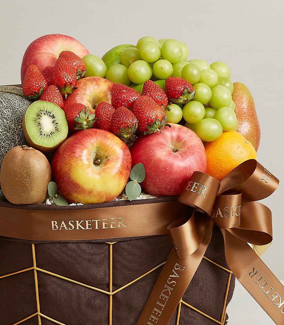 Dark brown wicker fruit basket with fresh apples, strawberries, grapes, kiwi and orange, gold ribbon detail
