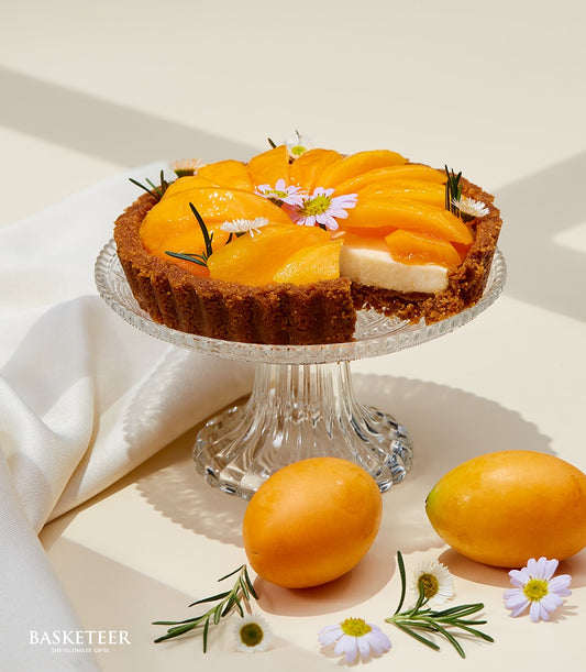 Golden mango cheese tart with creamy filling and fresh fruit slices on glass stand, artisan bakery gift