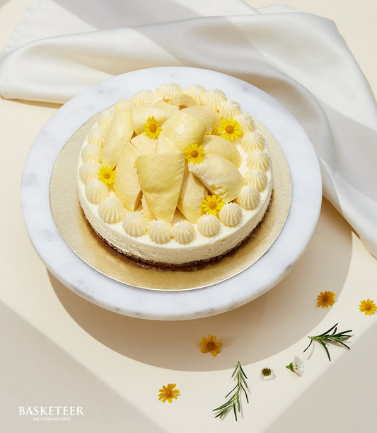 Premium durian cheesecake with fresh fruit and edible flowers on gold board, artisan celebration cake