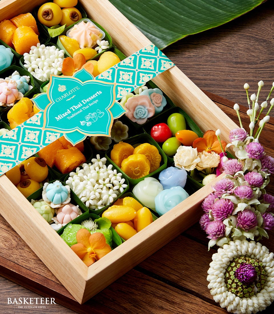 Wooden gift box of colorful Thai desserts in leaf containers with jasmine and purple flowers for Songkran celebration