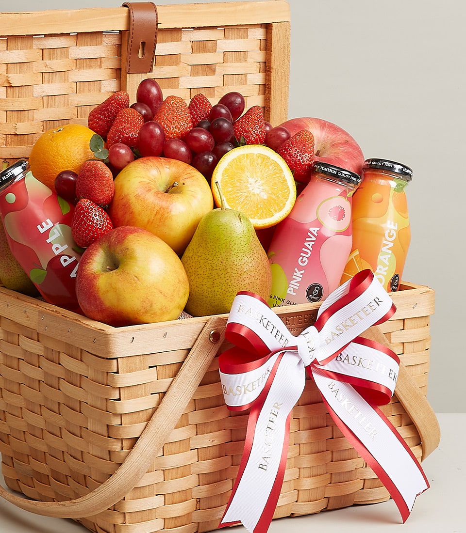 Woven wicker gift basket with fresh apples, pears, grapes, strawberries, and bottled fruit juices tied with white ribbon bow