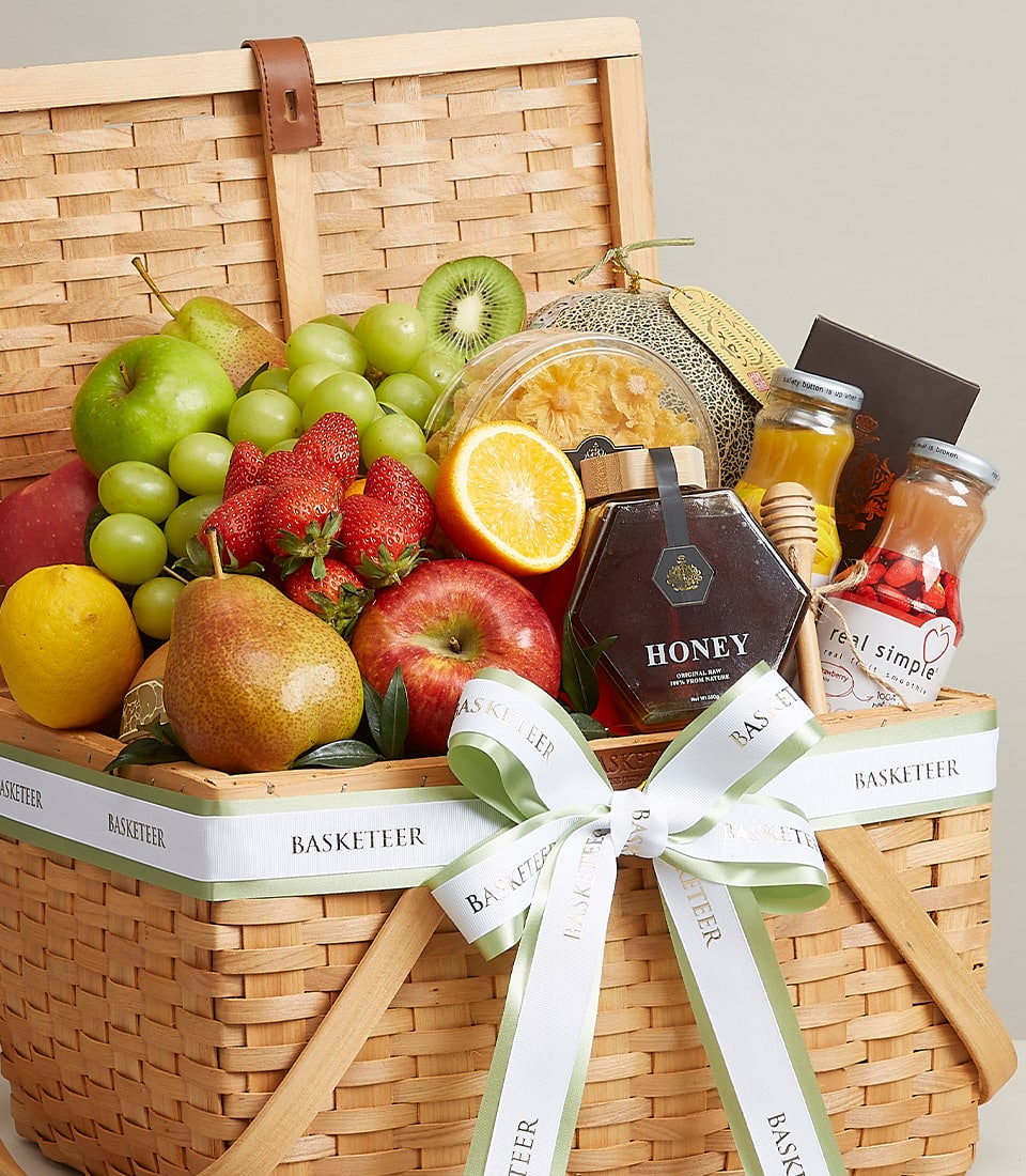 Wicker fruit gift basket with fresh apples, grapes, strawberries, pears, melon, honey jar and gourmet beverages