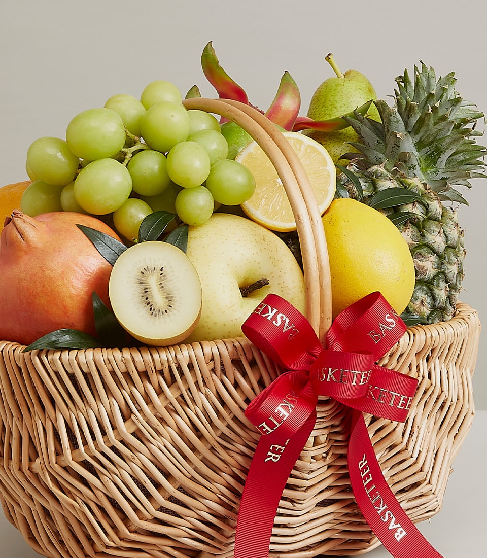 Woven wicker fruit basket with fresh grapes, pomegranate, kiwi, pears, and pineapple tied with red ribbon
