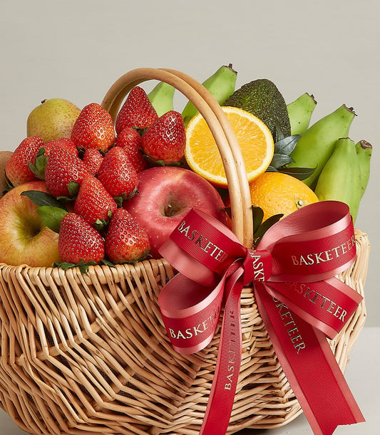 Woven wicker fruit basket with fresh strawberries, apples, pears, oranges, and avocado, tied with red Basketeer ribbon