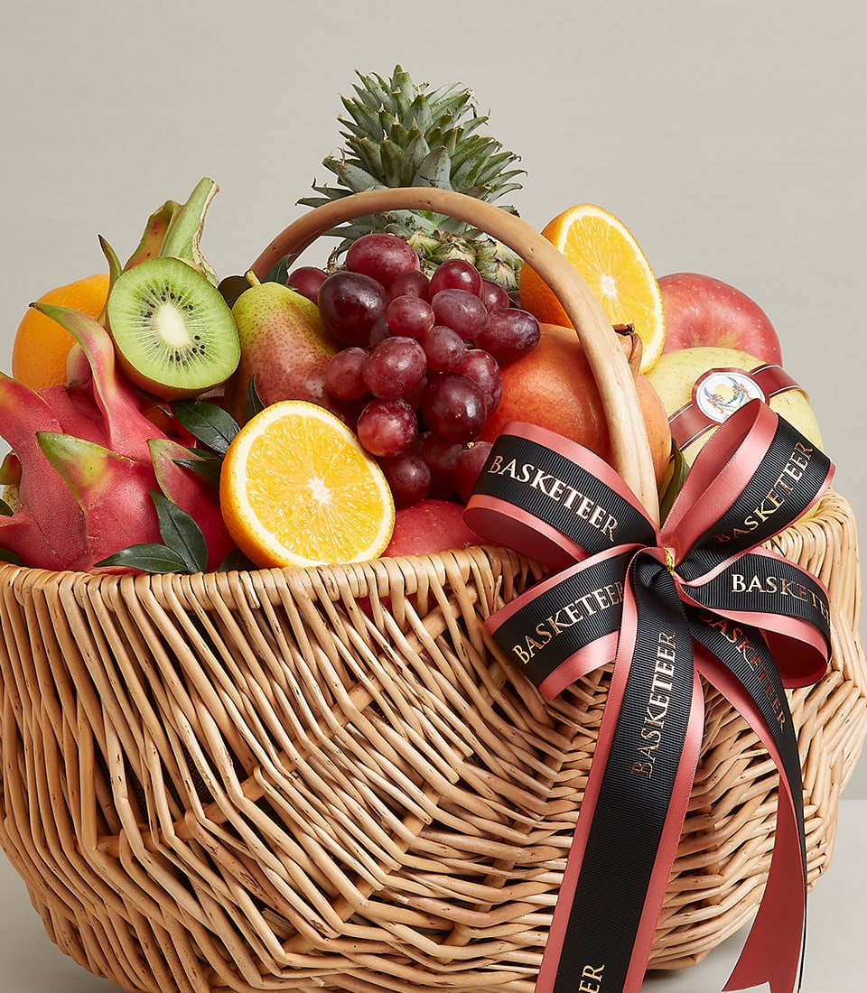 Woven wicker fruit basket with fresh grapes, apples, oranges, kiwi, dragon fruit and pineapple, tied with black ribbon bow