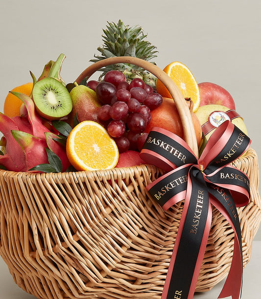 Woven wicker fruit basket with fresh grapes, apples, oranges, kiwi, dragon fruit and pineapple, tied with black ribbon bow