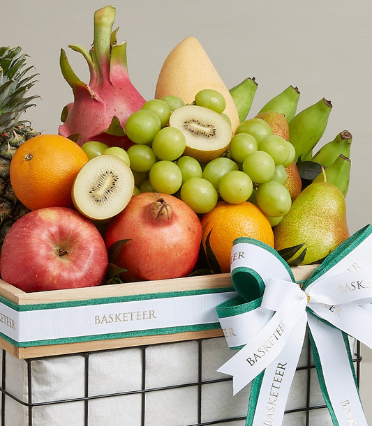 Vibrant tropical and orchard fruits arranged in wooden crate gift basket with white ribbon bow