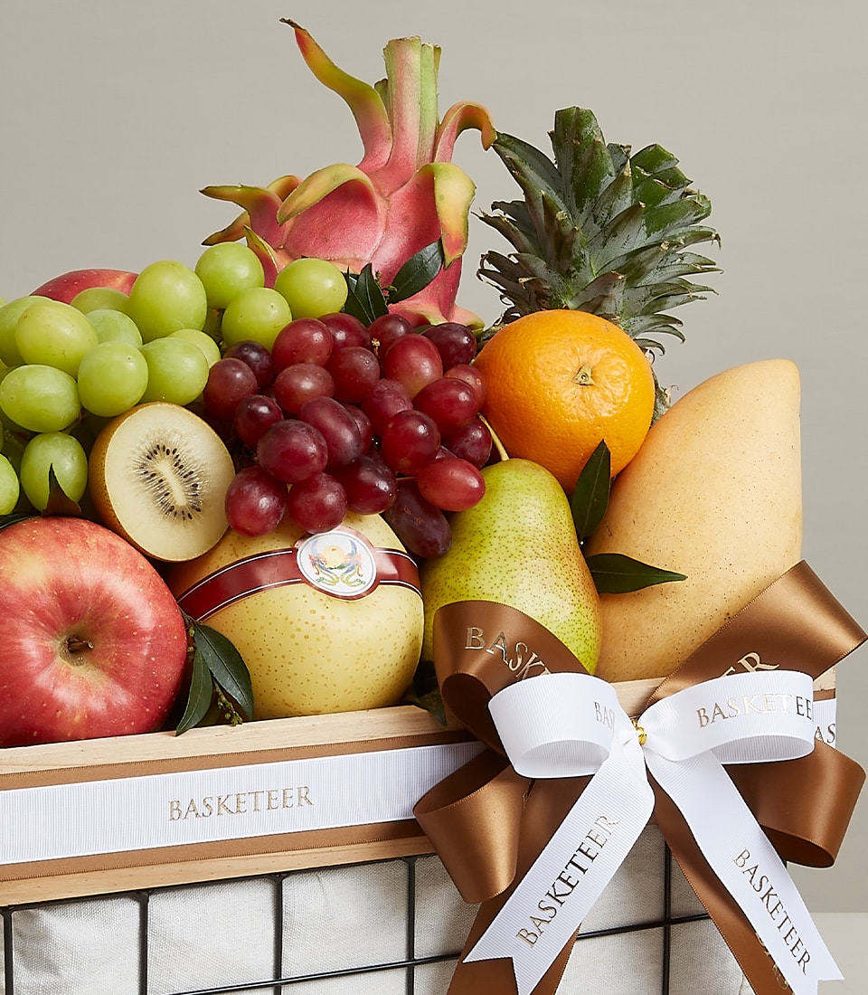Vibrant fruit gift basket with apples, grapes, mango, dragon fruit, and Asian pears in wooden frame with brown ribbon bow