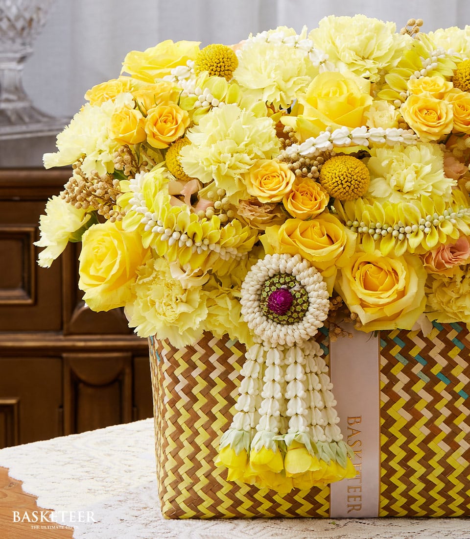 Vibrant yellow roses and carnations in woven basket with Thai phuang malai garland for Songkran celebration