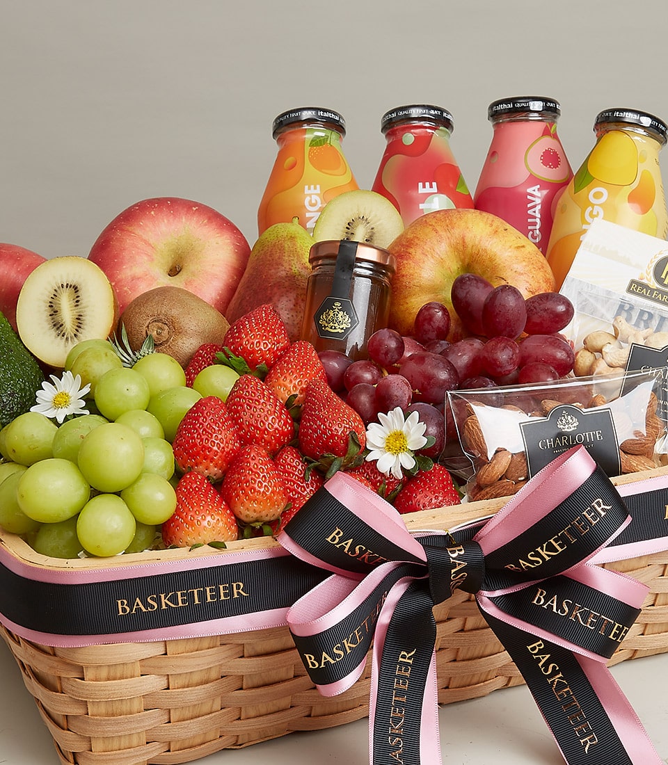 Woven wicker basket filled with fresh fruits, gourmet cheeses, nuts, and juices with black and pink ribbon bow