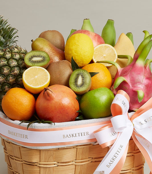 Regal woven fruit basket with pineapple, kiwi, citrus, apples, and tropical fruits tied with gold-accented ribbon