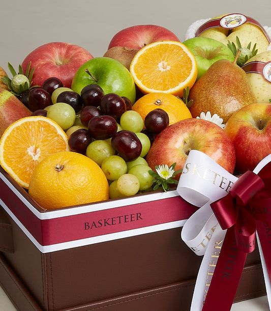 Luxury fruit gift basket with red apples, pears, oranges, and grapes in dark brown leather container with red ribbon