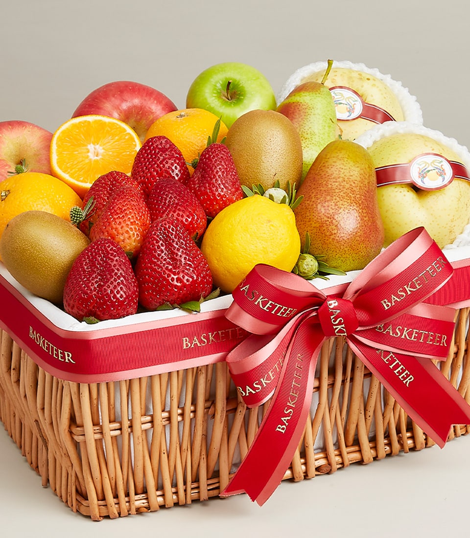 Woven wicker fruit basket with strawberries, oranges, apples, kiwi and pears tied with red Basketeer ribbon