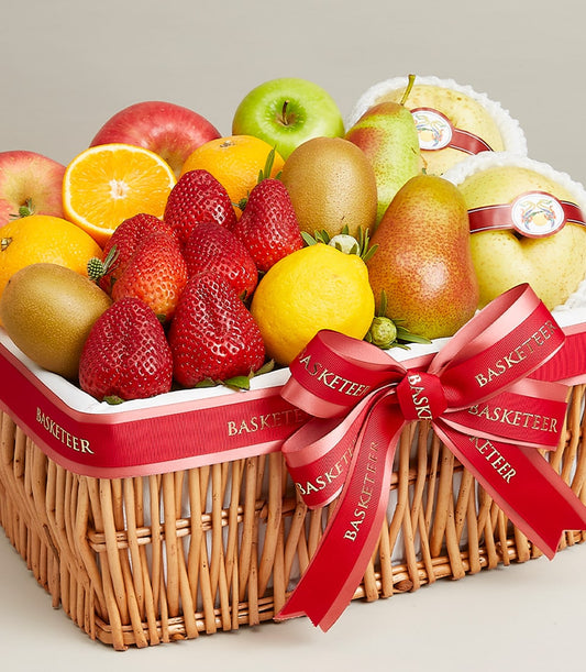 Woven wicker fruit basket with strawberries, oranges, apples, kiwi and pears tied with red Basketeer ribbon