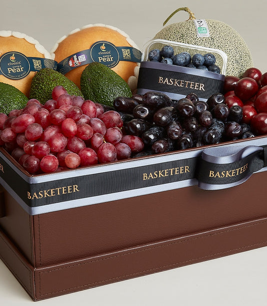 Luxury fruit selection box with pears, avocados, grapes, blueberries, and melon in brown leather gift box with black ribbon