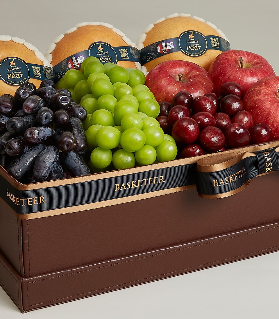 Premium brown leather fruit gift box with pears, grapes, apples, and cherries, topped with black and gold Basketeer ribbon