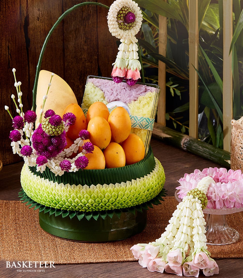 Thai fruit and floral gift basket with mango, sticky rice, and white purple blooms for Songkran