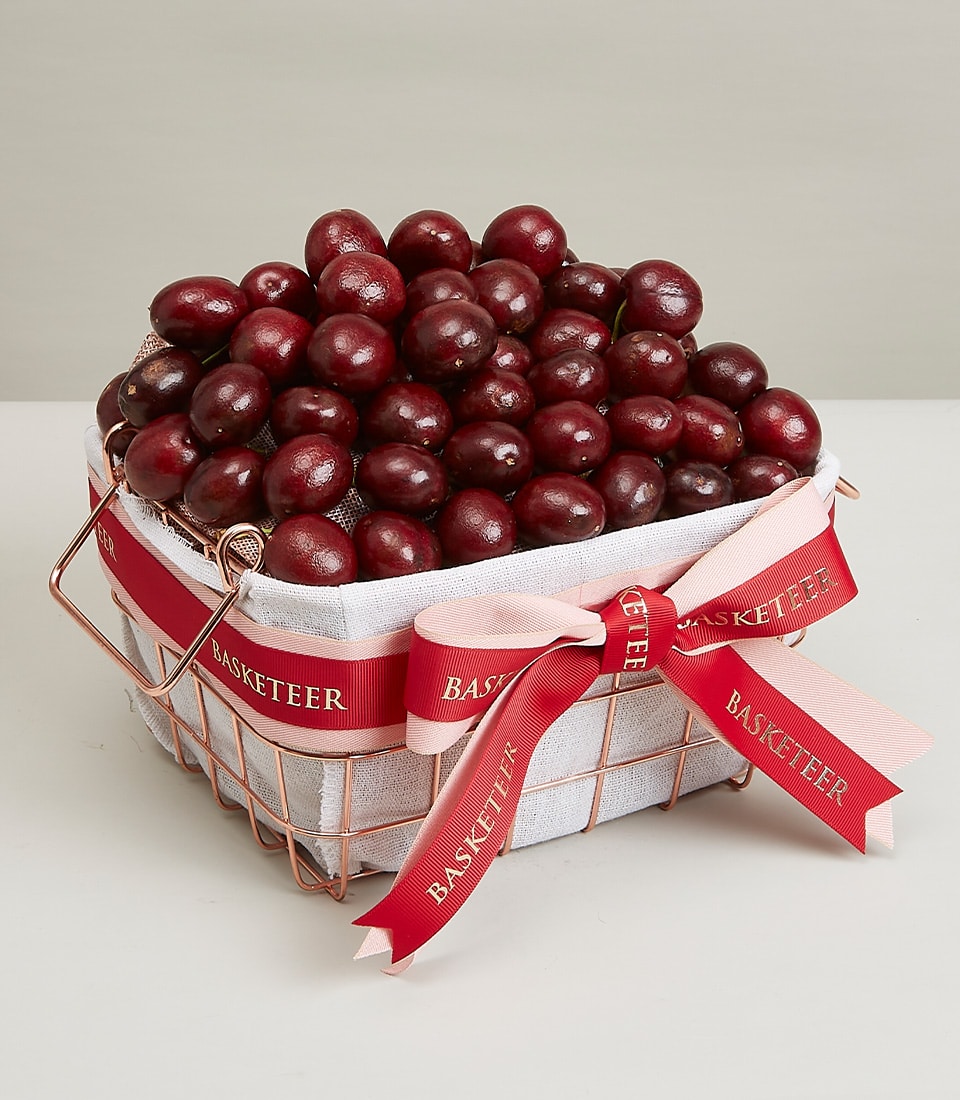 Rose gold wire basket filled with dark red cherries and berries, tied with pink and deep red ribbons