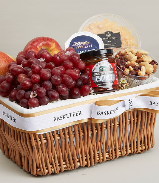 Gourmet fruit and cheese gift basket with grapes, pear, apple, Camembert, nuts, and chutney in wicker