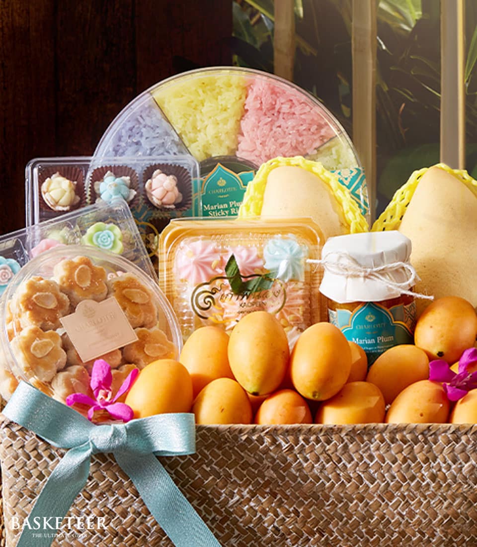Woven gift basket with Thai fruits, desserts, and colorful meringues tied with blue ribbon and pink orchid for New Year
