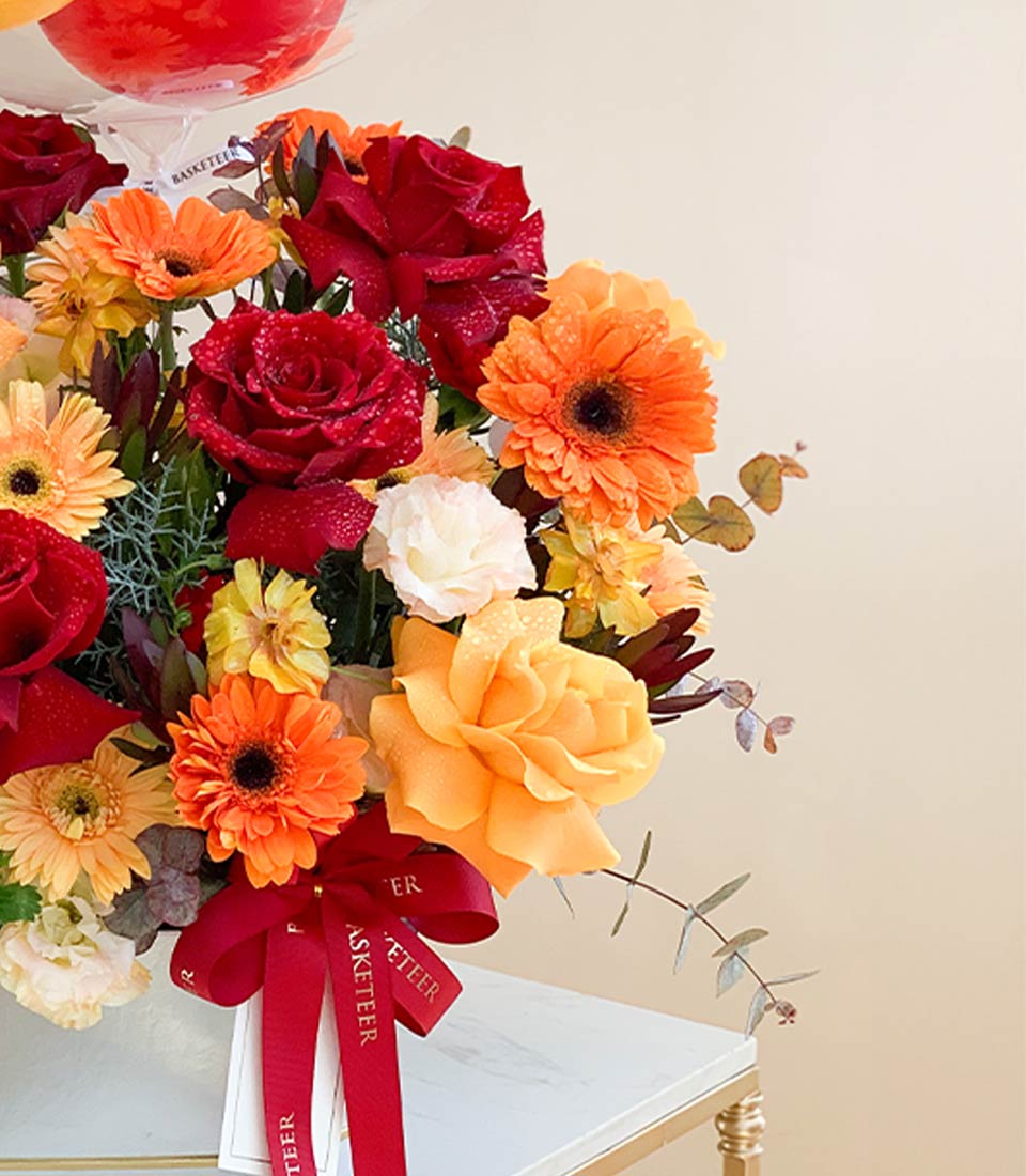 Vibrant red and orange roses with gerbera daisies and balloons in white gold-accented vase, birthday flower gift