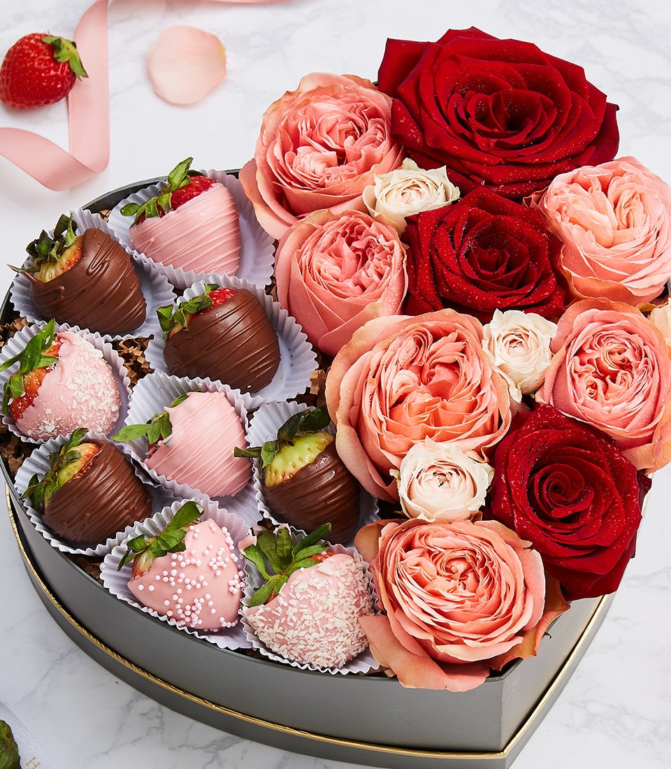 Heart-shaped luxury gift box with chocolate-dipped strawberries and fresh roses in red, coral, and pink