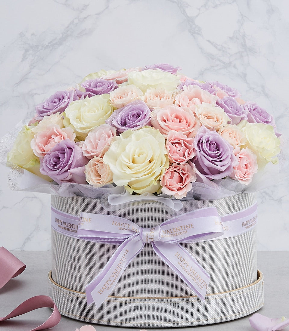 Pastel lavender, pink, and white roses in round gift box with gold rim, fresh flower arrangement for birthdays and