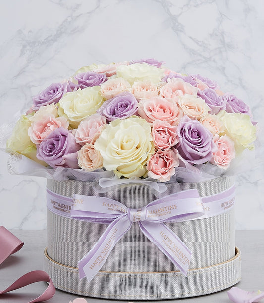 Pastel lavender, pink, and white roses in round gift box with gold rim, fresh flower arrangement for birthdays and
