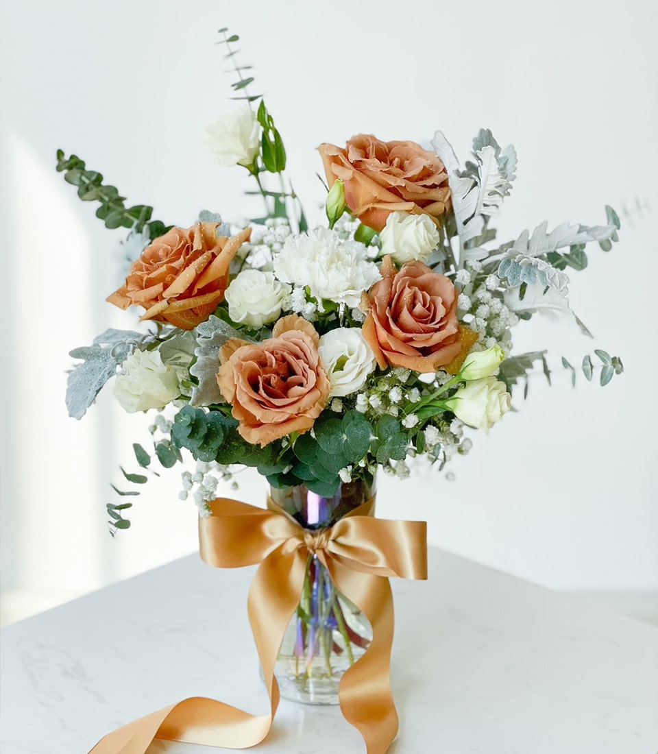 Rustic burnt orange and dusty rose arrangement with white baby's breath and eucalyptus in clear glass vase with golden ribbon