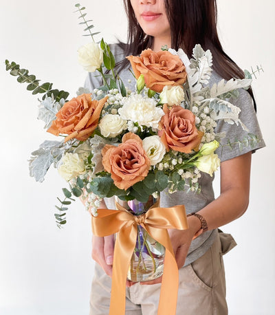 Rustic burnt orange and dusty rose bouquet with white carnations and eucalyptus in clear vase with golden ribbon