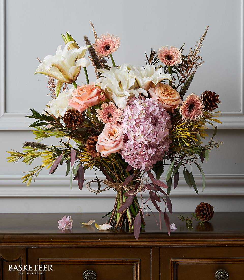 Premium rustic floral arrangement with white lilies, peach roses, and pink hydrangeas with pinecones and natural twine