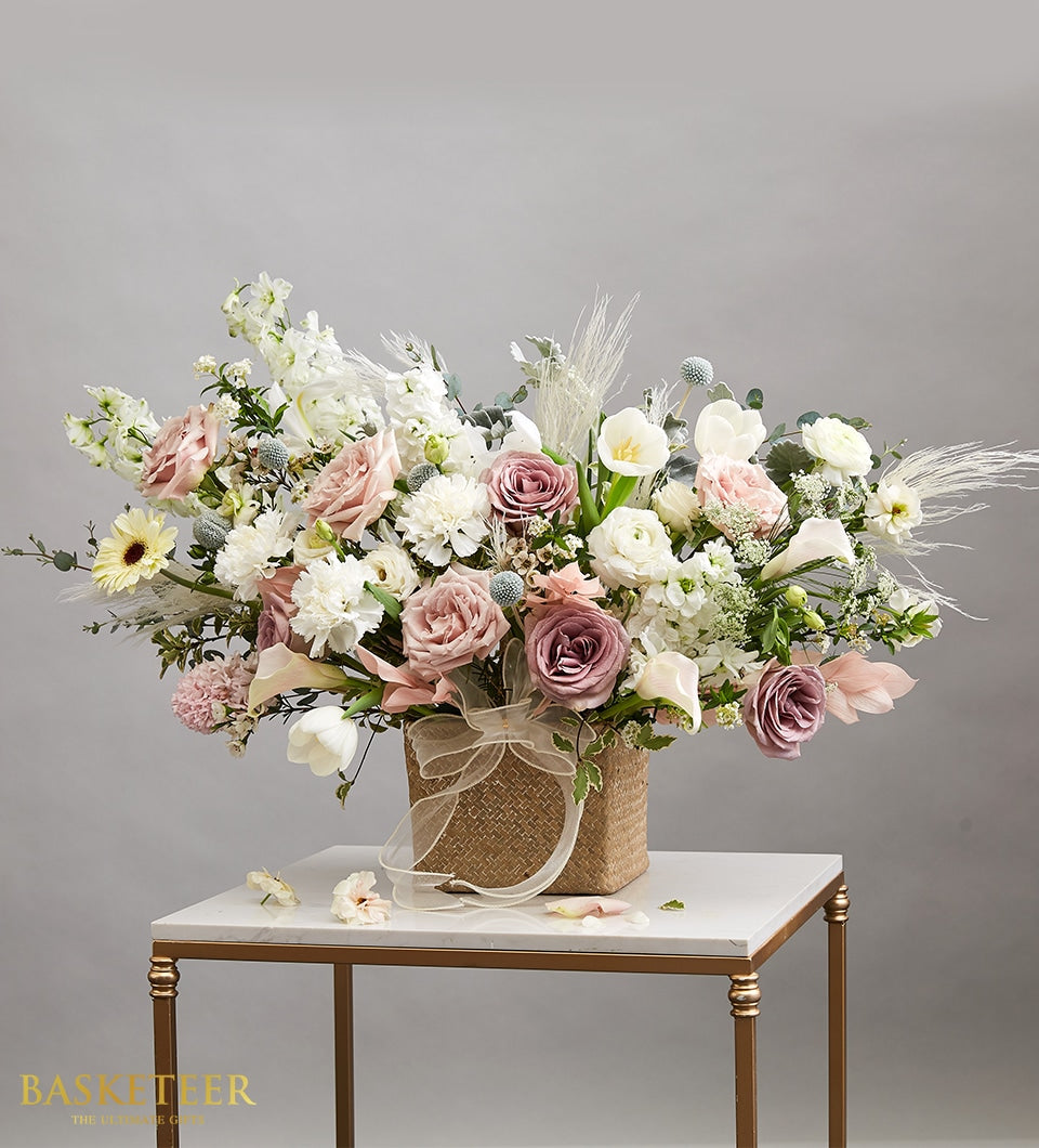 Elegant white and blush rose bouquet with tulips and calla lilies in woven basket, gold ribbon accent