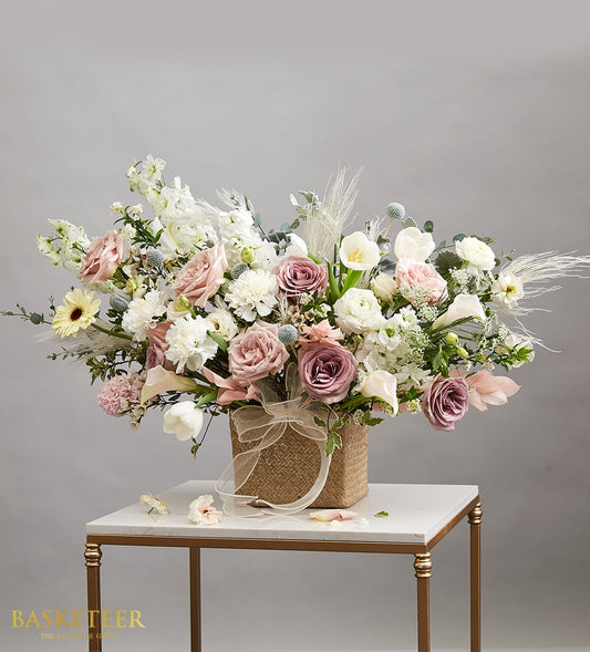 Elegant white and blush rose bouquet with tulips and calla lilies in woven basket, gold ribbon accent