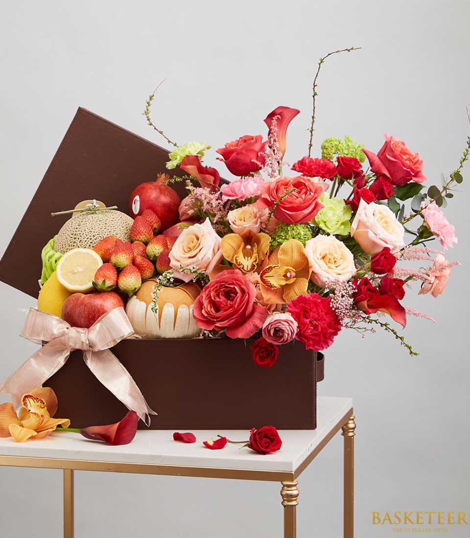 Luxury dark brown gift box with fresh tropical fruits, vibrant roses and orchids, tied with pink satin ribbon