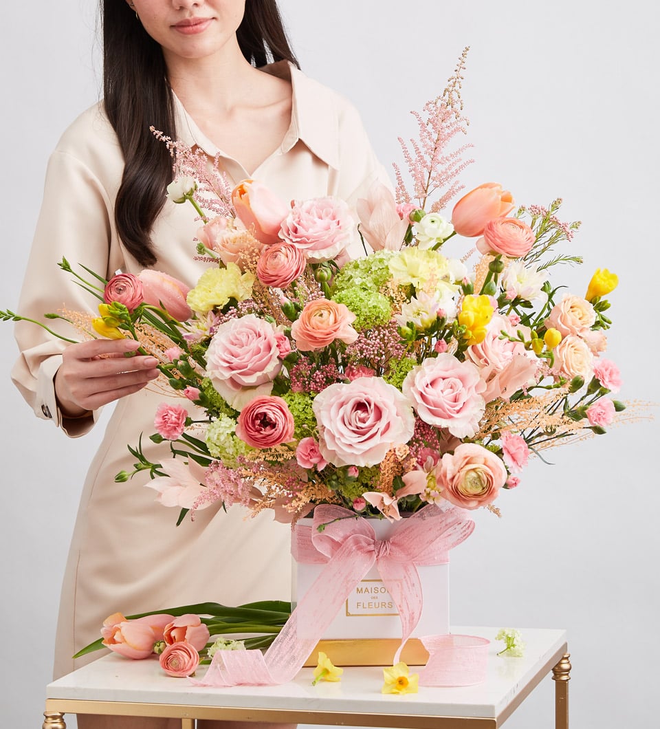 Pink roses, peach ranunculus, and hydrangeas in white gift box with gold satin ribbon