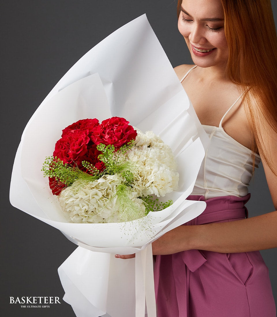 Red and white carnation and hydrangea bouquet with green foliage in white paper wrapping