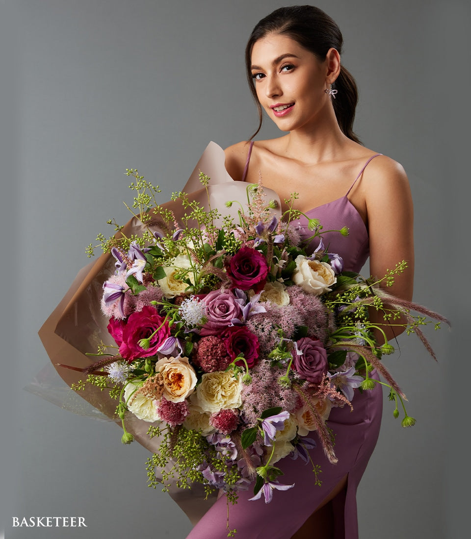 Luxe mixed rose bouquet in red, pink, and cream with purple accents, held by woman in lavender slip dress
