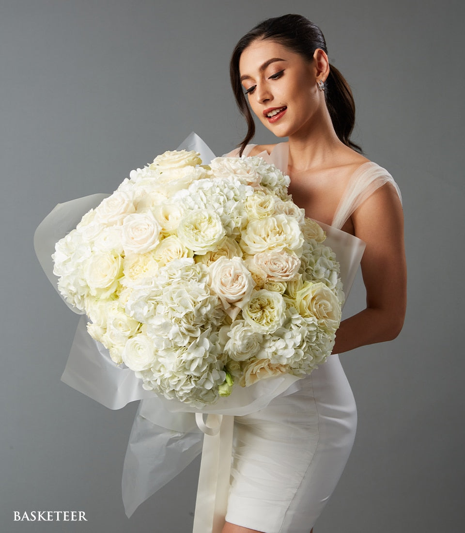 Elegant white rose and hydrangea Valentine's Day bouquet with cream accents, wrapped in white paper
