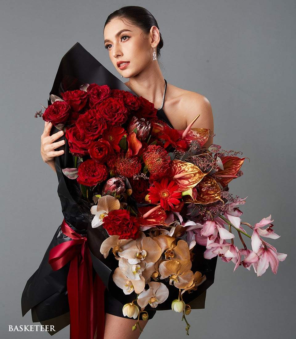 Luxurious red roses and protea bouquet with gold accents, wrapped in black paper with red ribbon for Valentine's Day