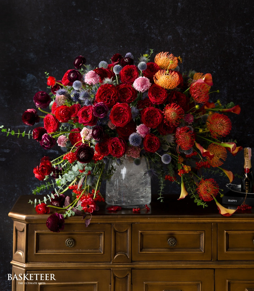 Fiery Passion luxury floral arrangement with red roses, ranunculus, and orange protea in clear glass vase
