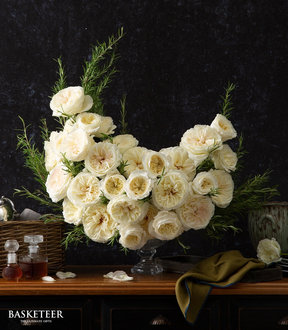 White and cream rose vase arrangement with dark green foliage in clear glass bowl, luxury gift hamper styling