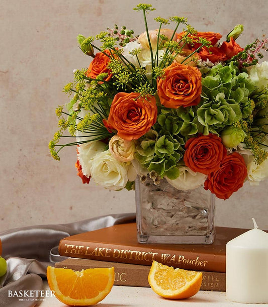 Vibrant mixed rose and hydrangea arrangement in glass cube vase with orange, white, and green blooms