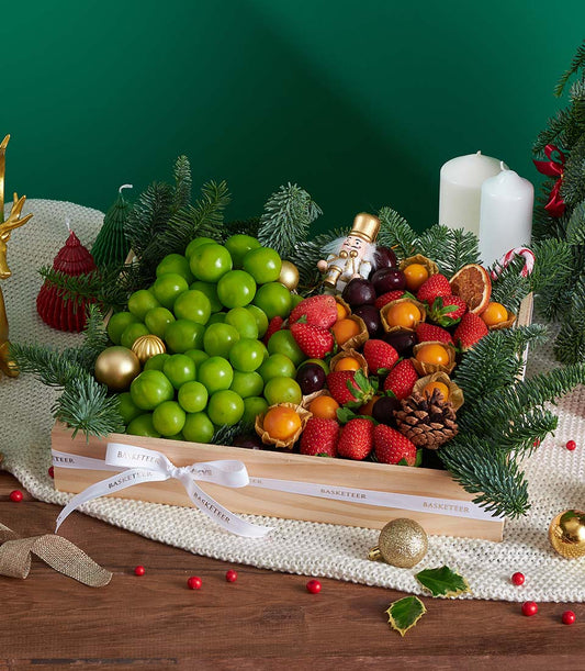 Premium festive fruit gift box with Shine Muscat grapes, strawberries, and cherries nestled among gold ornaments and pine