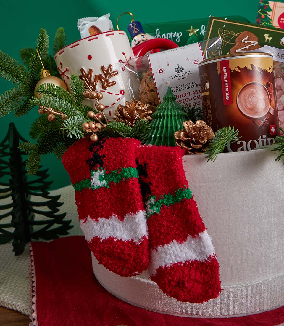 Festive Christmas gift basket with gold reindeer mug, hot chocolate, artisan cookies, and red striped socks