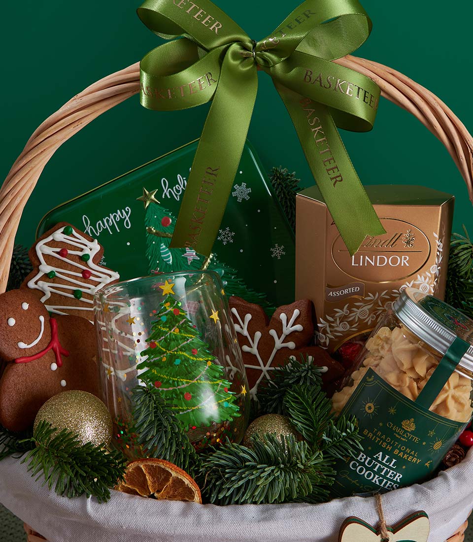 Festive Christmas gift basket with gourmet cookies, Lindor chocolates, and gingerbread treats nestled in greenery and gold