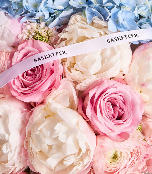 Pastel Harmony mixed bouquet with pink roses, white peonies, and blue hydrangeas, tied with white ribbon