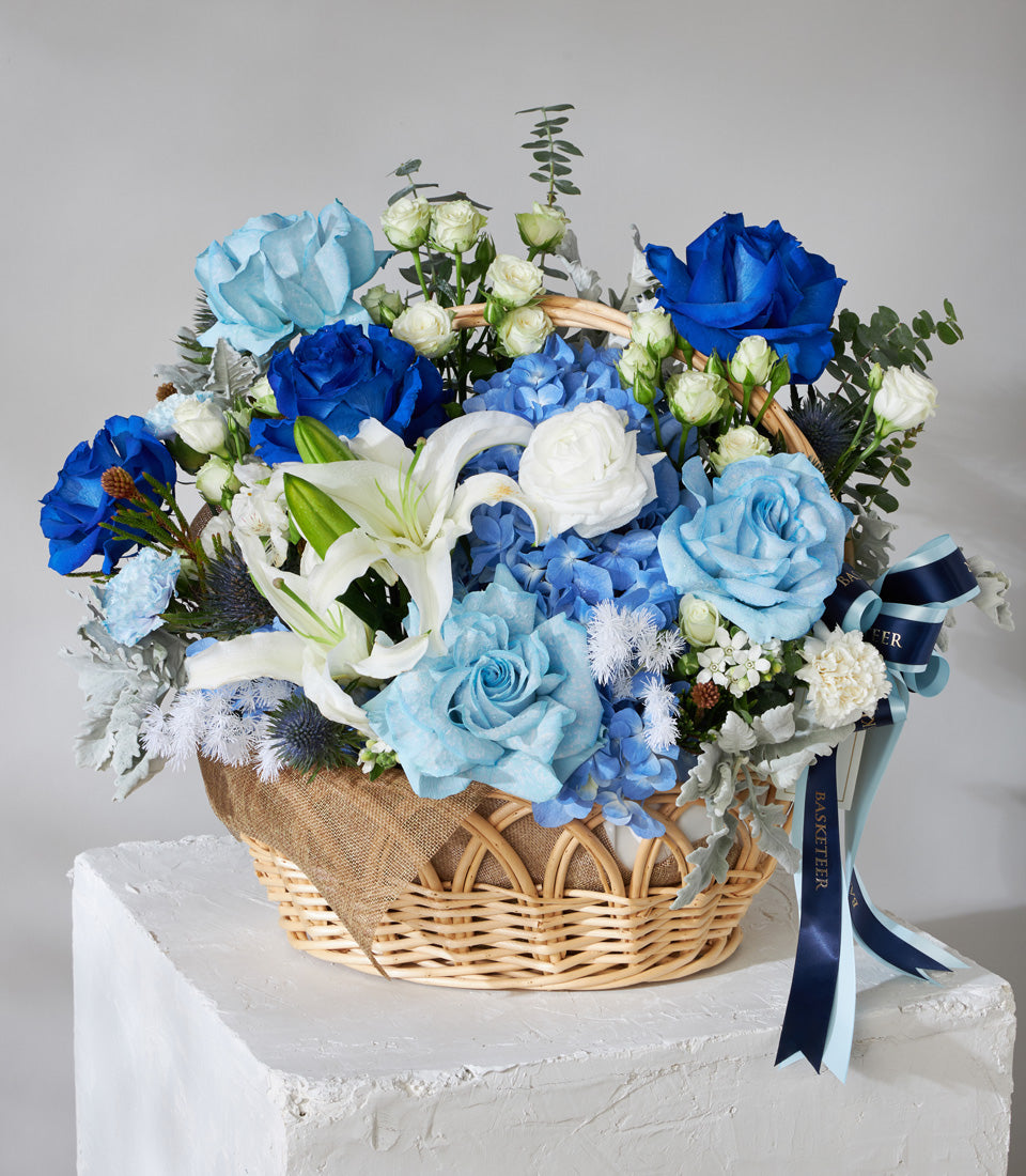 Blue and white rose basket with hydrangeas, lilies, and silver foliage in woven wicker