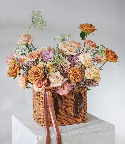 Caramel and blush roses with lilac filler flowers in woven wicker basket